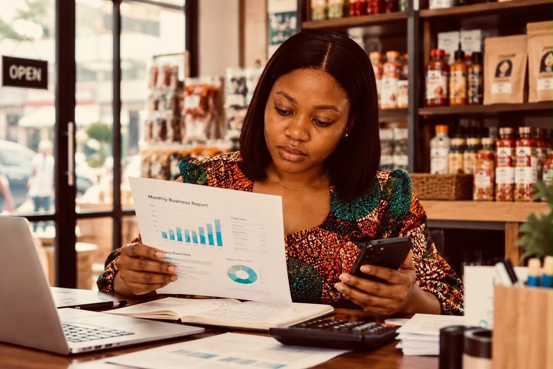 A business owner reading her monthly report with her phone and calculator