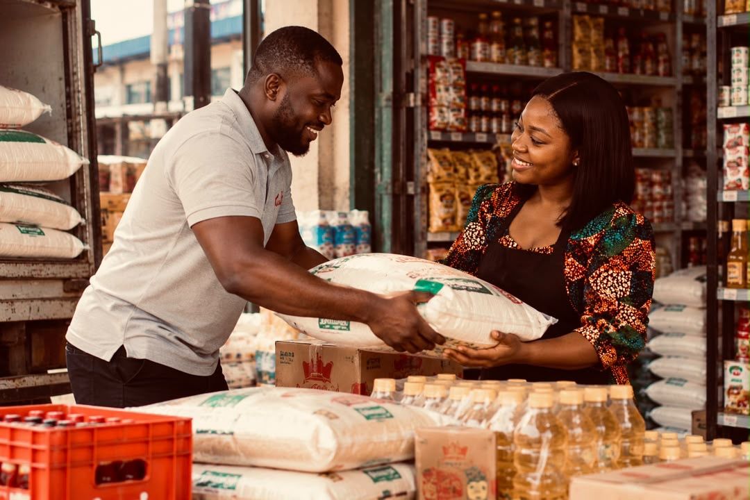A supplier handing a bag of rice to a provisions shop owner